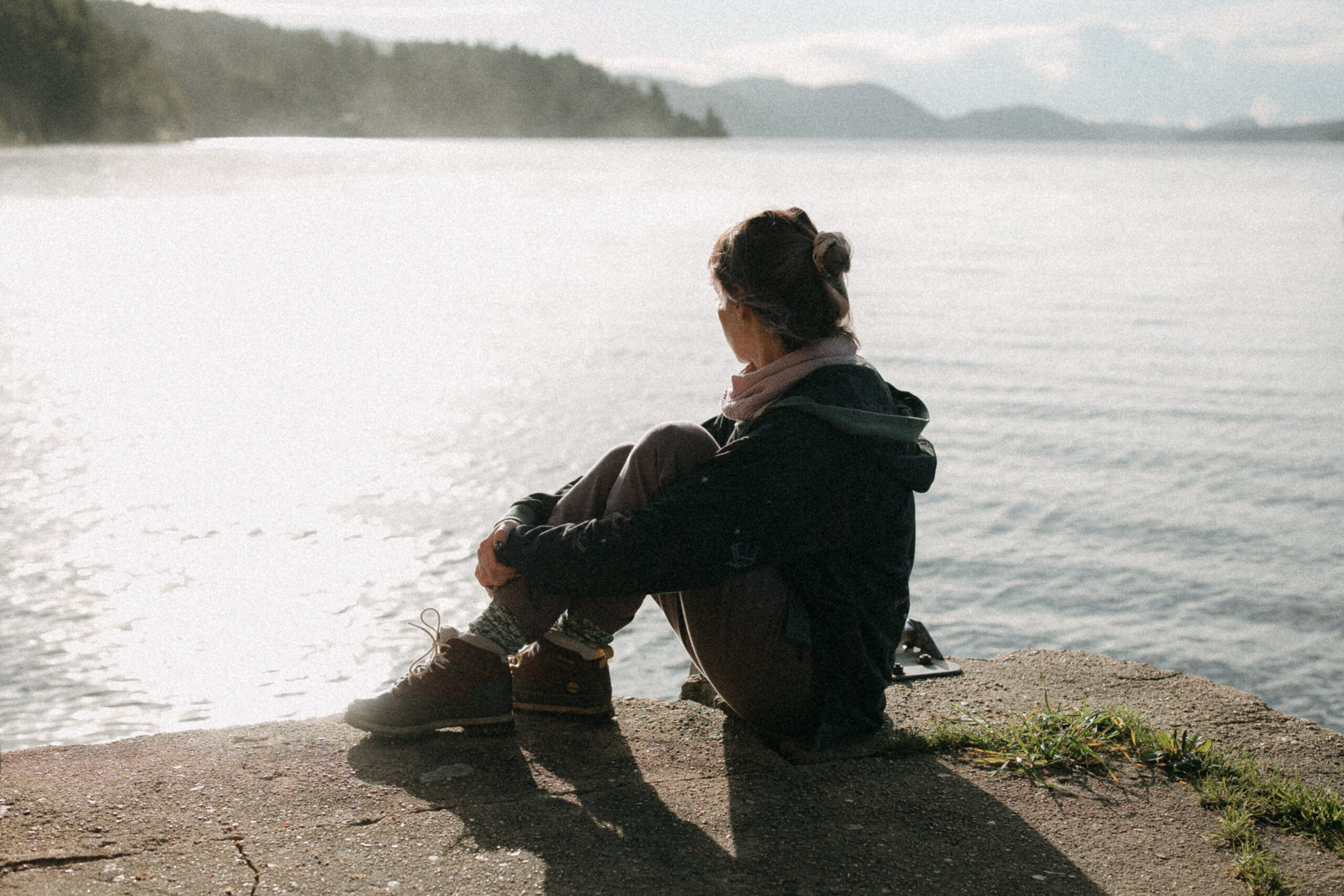 A woman sits peacefully by a sunlit lake in Ferny Tales clothing, looking toward the horizon — a personal portrait from the creator sharing the brand’s sizing philosophy.
