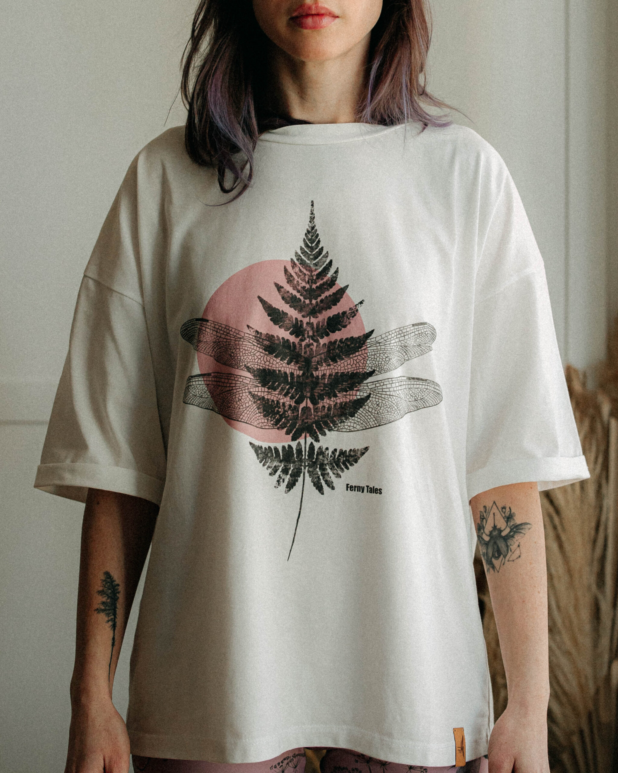 Woman in a light cream tee with a large central fern print, arms relaxed by her sides.