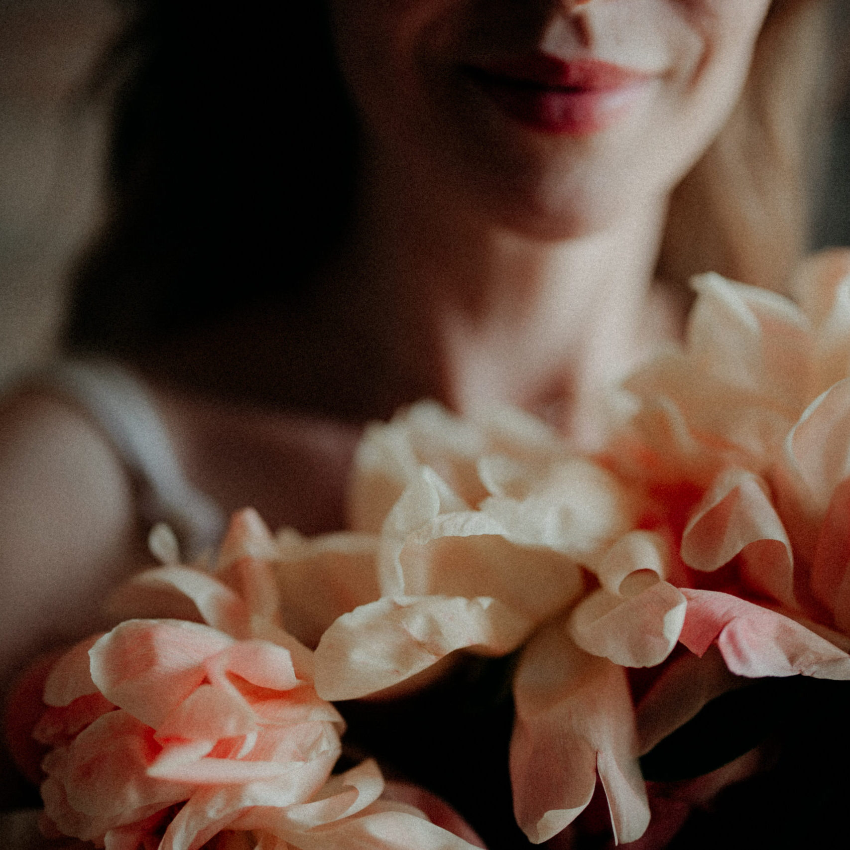 Soft close-up of a woman’s smile and collarbone, holding a bundle of peach garden petals in gentle morning light.