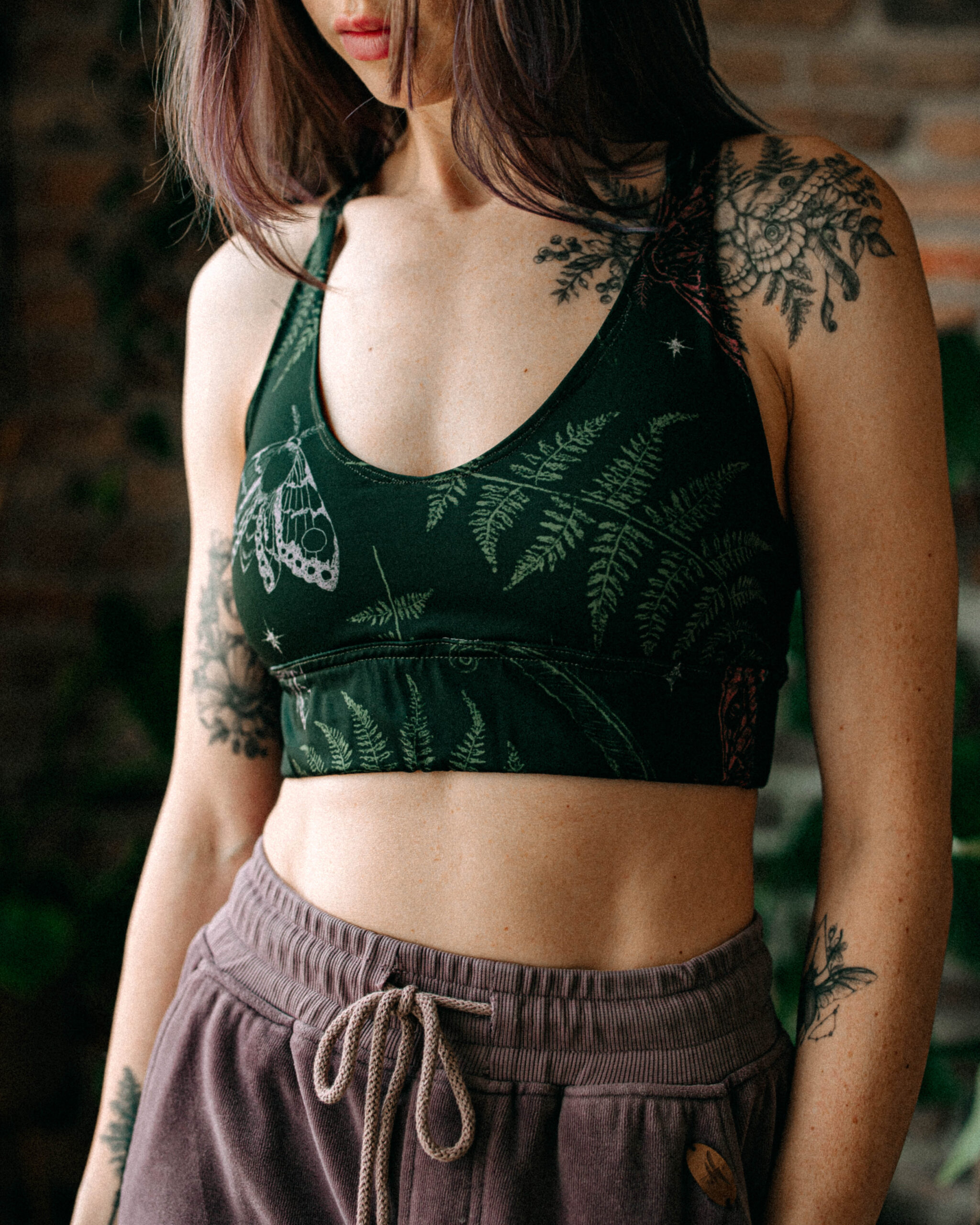 Woman wearing a dark green printed sport top with moth and fern patterns.