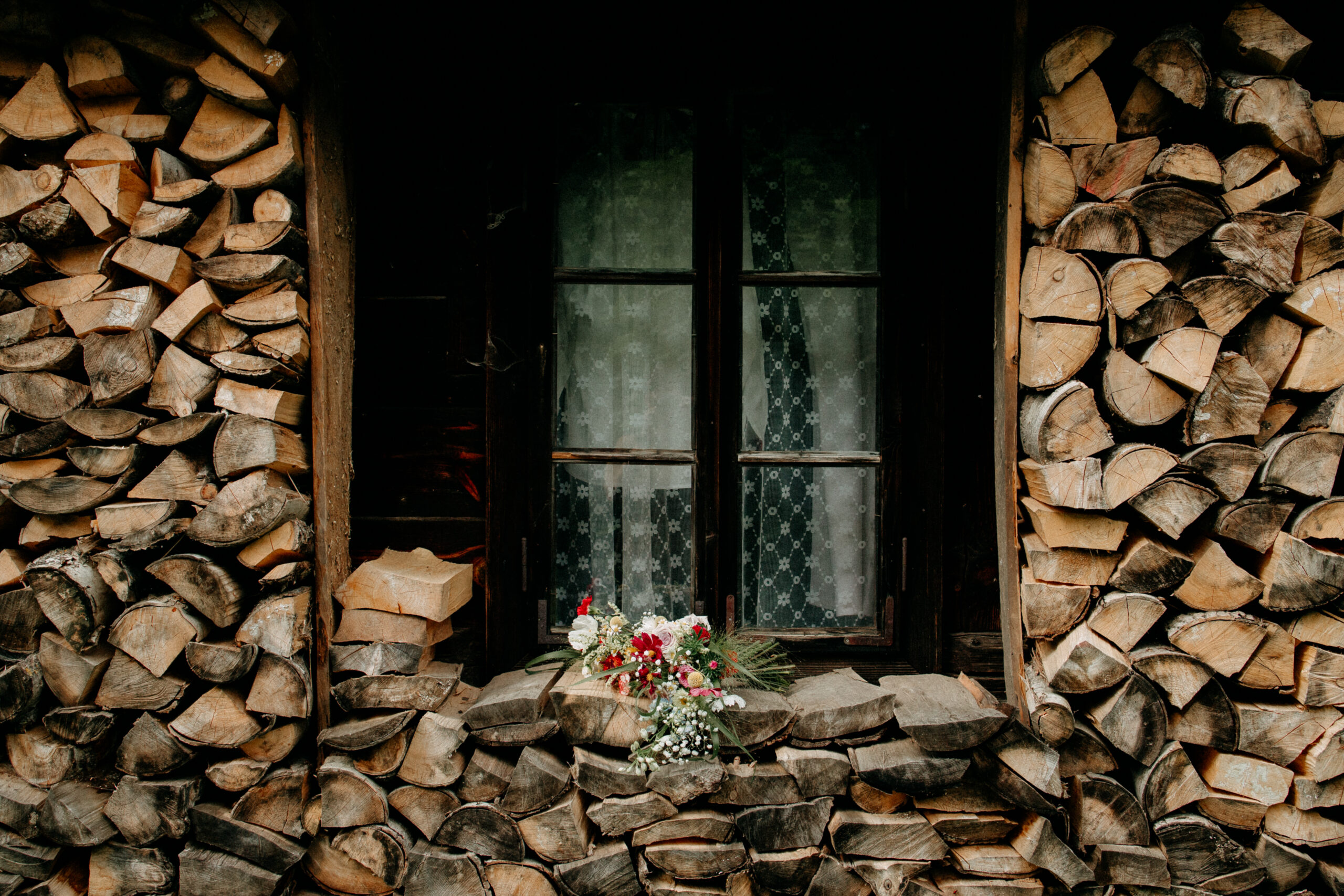 Floral bouquet resting on stacked firewood in front of a dark window with lace curtains — Ferny Tales preorder information hero image.