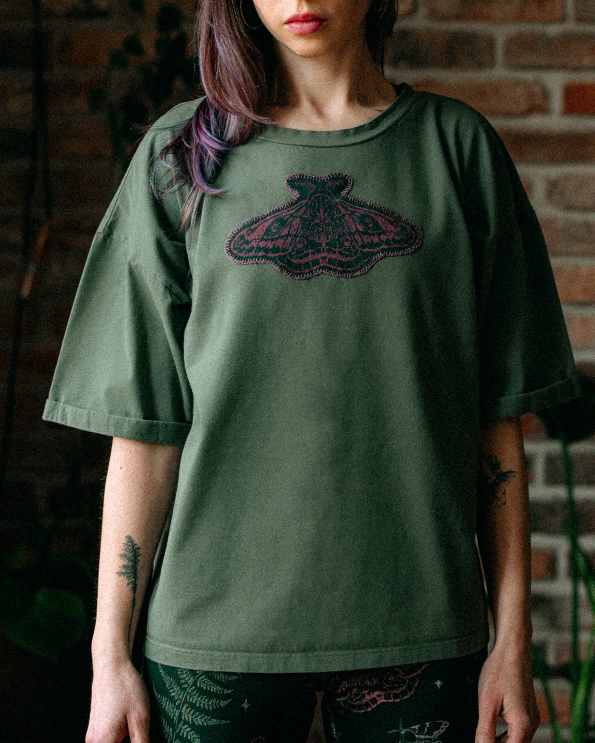 Woman wearing an oversized khaki green tee with a stitched moth design.