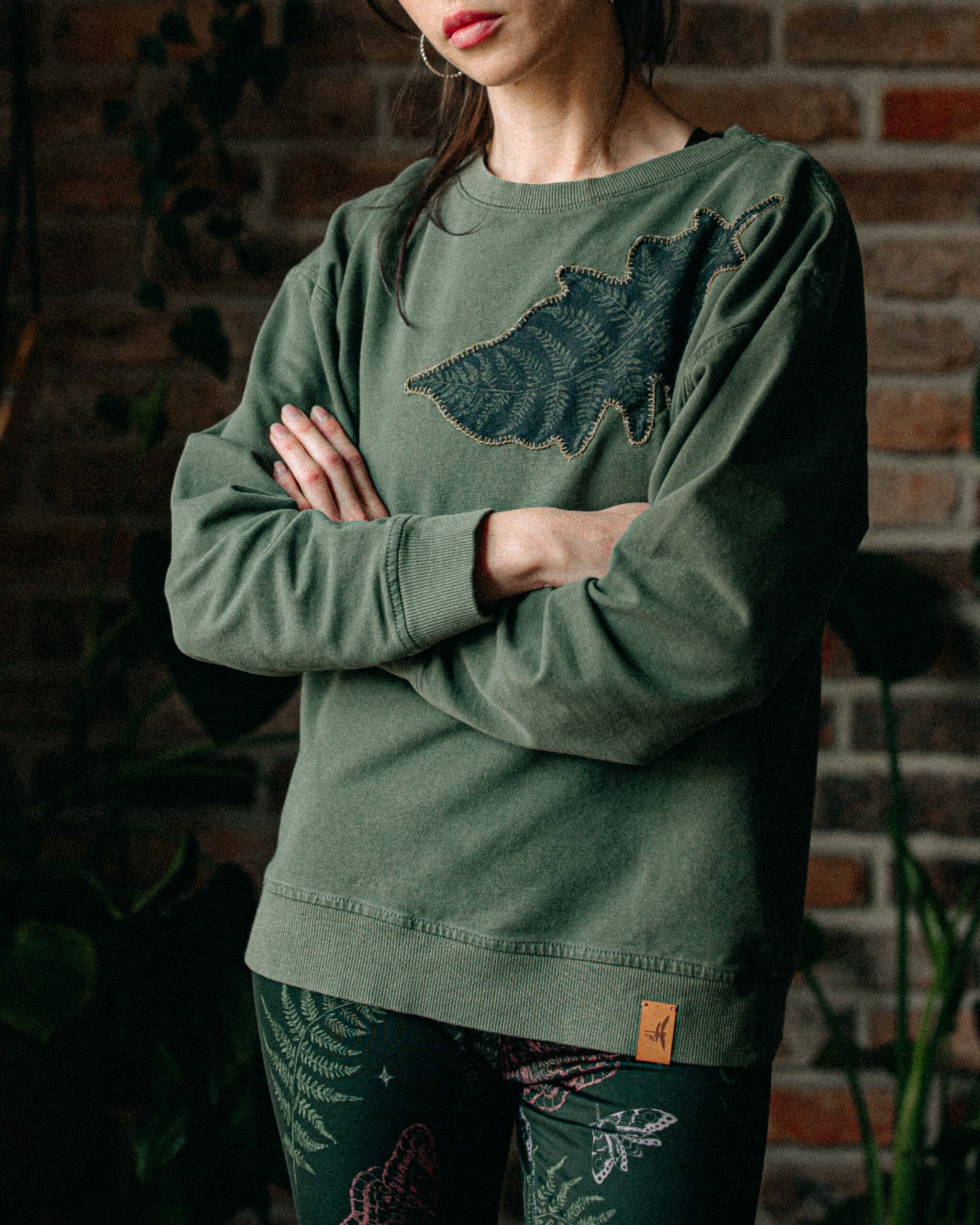 Model softly crossing arms, wearing the Ferniest Sweatshirt against a dark background.
